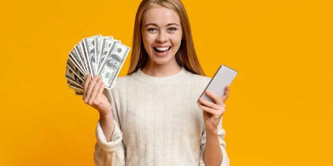 در تصویر دختری با یک دست پر از پول و دست دیگرش گوشی موبایل را نشان می‌دهد. در این مطلب اشاره می‌کنیم که می‌توان تنها با یک گوشی به کسب درآمد در فضای آنلاین پرداخت.