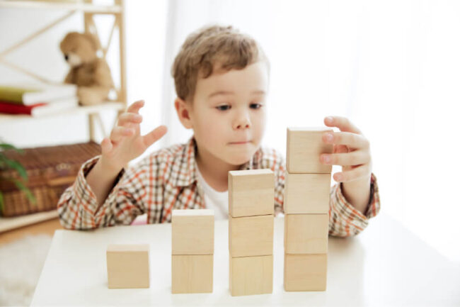 یک کودک پسر در حال بازی کردن با مکعب‌های کرمی. مشاوره کودک برای بچه‌ها در دوران کودکی بسیار اهمیت دارد.